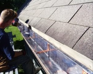 Man installing lead-coated copper gutters into shingle roof.