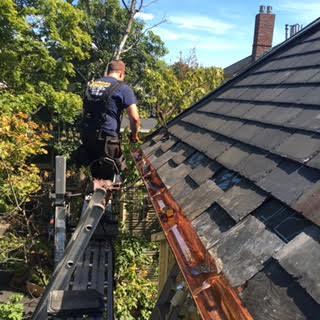 One of our crew members works his way down the gutter line to ensure that it has been installed properly. You can see the layers of slates which have been removed to ensure that the gutter is properly tied into the roof.