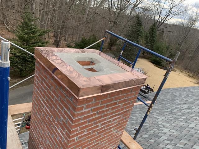 Installing a copper chimney cap onto the chimney.