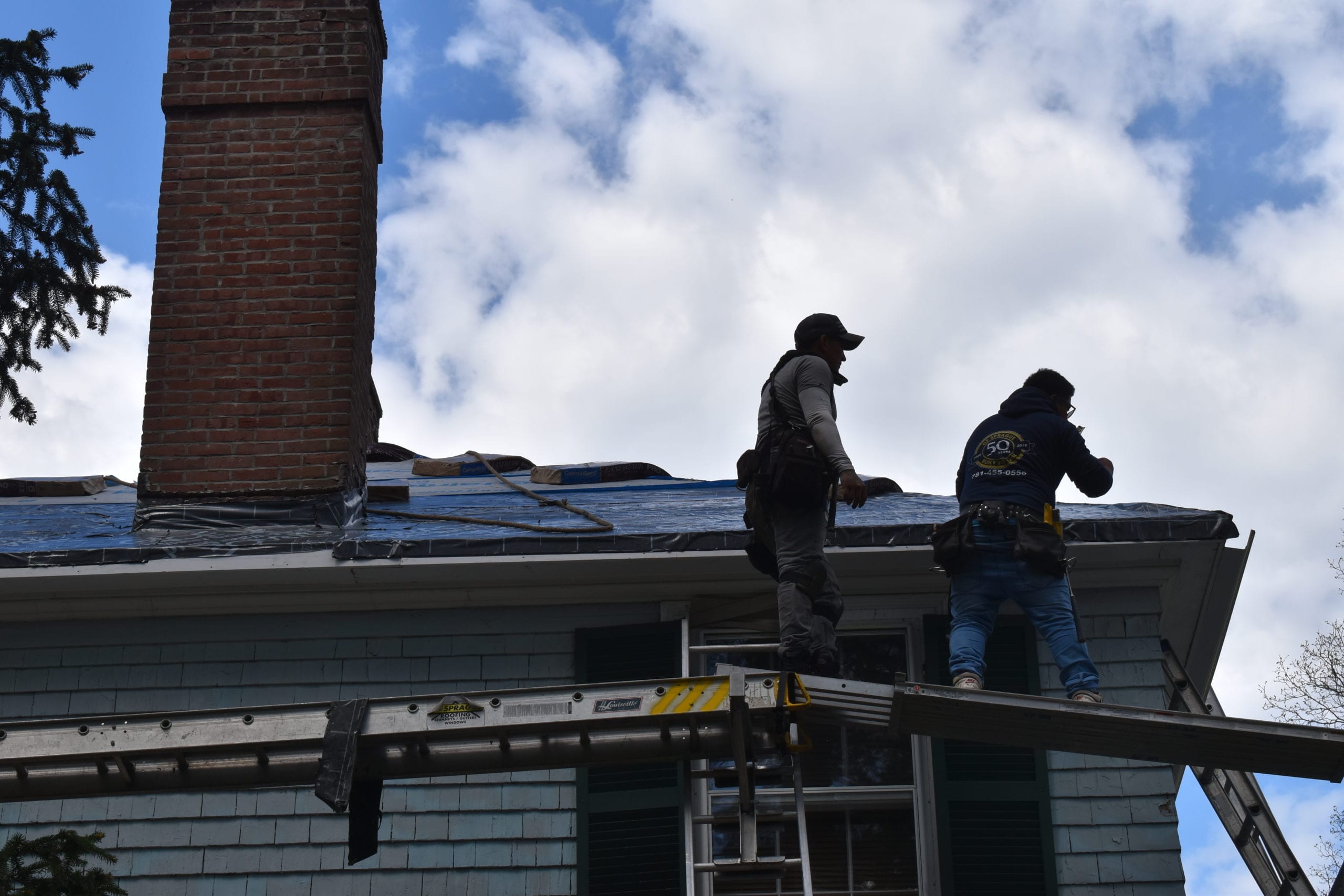 two roofing contractors work on a roof on a house